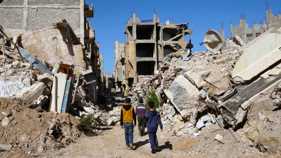Three boys walk down a path through a bombed-out urban area