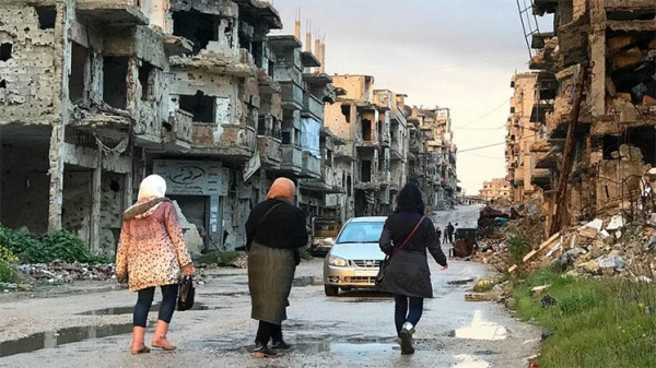 Three women walk down a street full of bombed-out buildings
