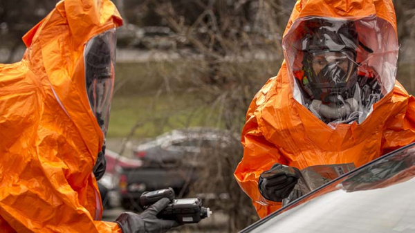 Two people in orange hazmat suits inspect a car 